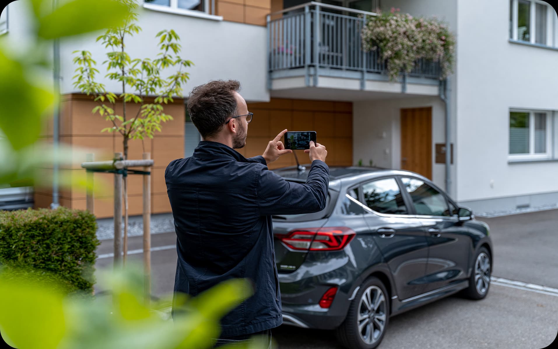 Person dokumentiert mit dem Smartphone ein falsch geparktes Fahrzeug vor einem Wohnhaus