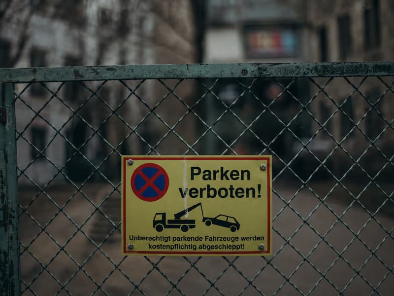 Yellow no-parking sign on a wire fence warning that unauthorised vehicles are towed at the owner’s expense