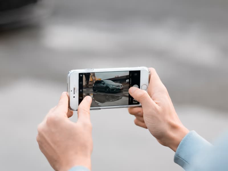 Hands holding a smartphone to photograph a parked car