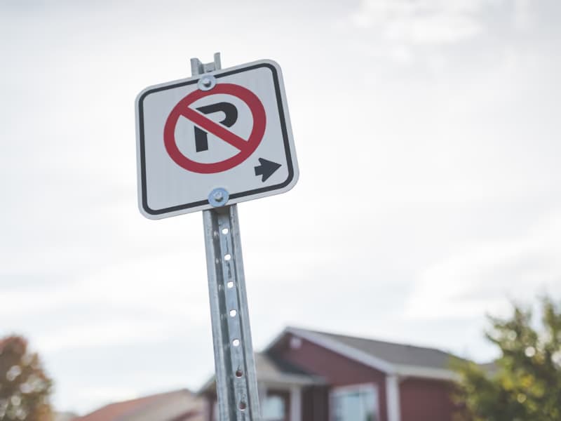 No-parking sign with a directional arrow on a post against a cloudy sky