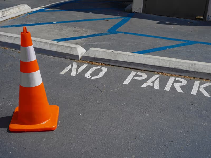 Orange Verkehrsleitkegel auf einer blau markierten Parkfläche mit Aufschrift «no park» auf dem Asphalt