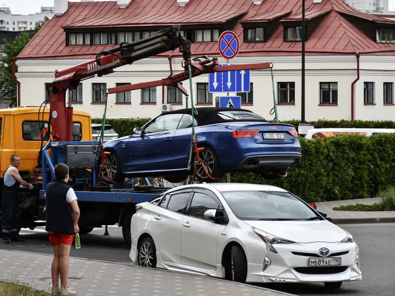 Crane tow truck lifting a blue car from the roadside