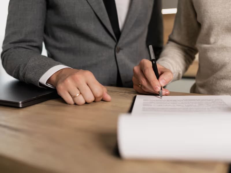 Person in a suit signing a contract at a wooden table