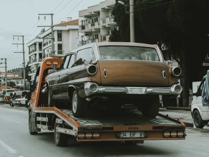 Brown vintage car on the bed of a tow truck in a city street