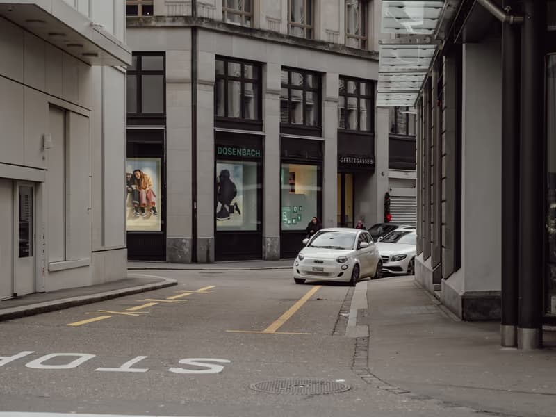 White car parked on a street corner outside shop windows in the city centre